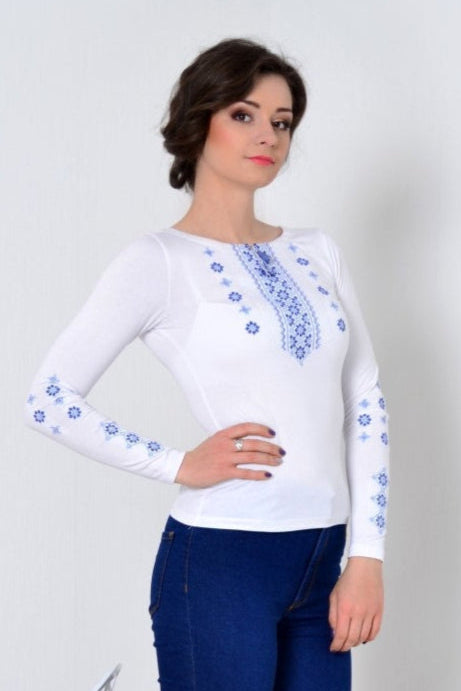 Elegante blusa bordada de manga larga con motivos folclóricos ucranianos en azul sobre una tela blanca suave. Un diseño atemporal que combina artesanía tradicional con moda moderna, ideal para eventos culturales o un look sofisticado diario